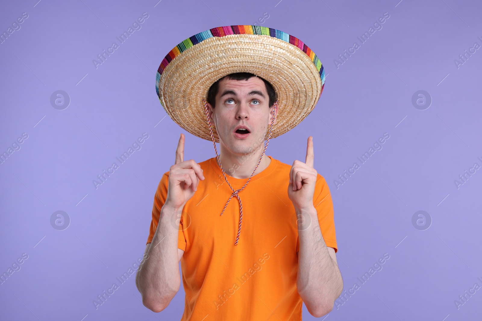 Photo of Young man in Mexican sombrero hat pointing at something on violet background