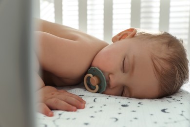 Photo of Cute little baby with pacifier sleeping in crib, closeup