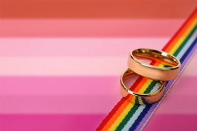 Image of Golden wedding rings and rainbow ribbon on background in color of lesbian flag, space for text.
