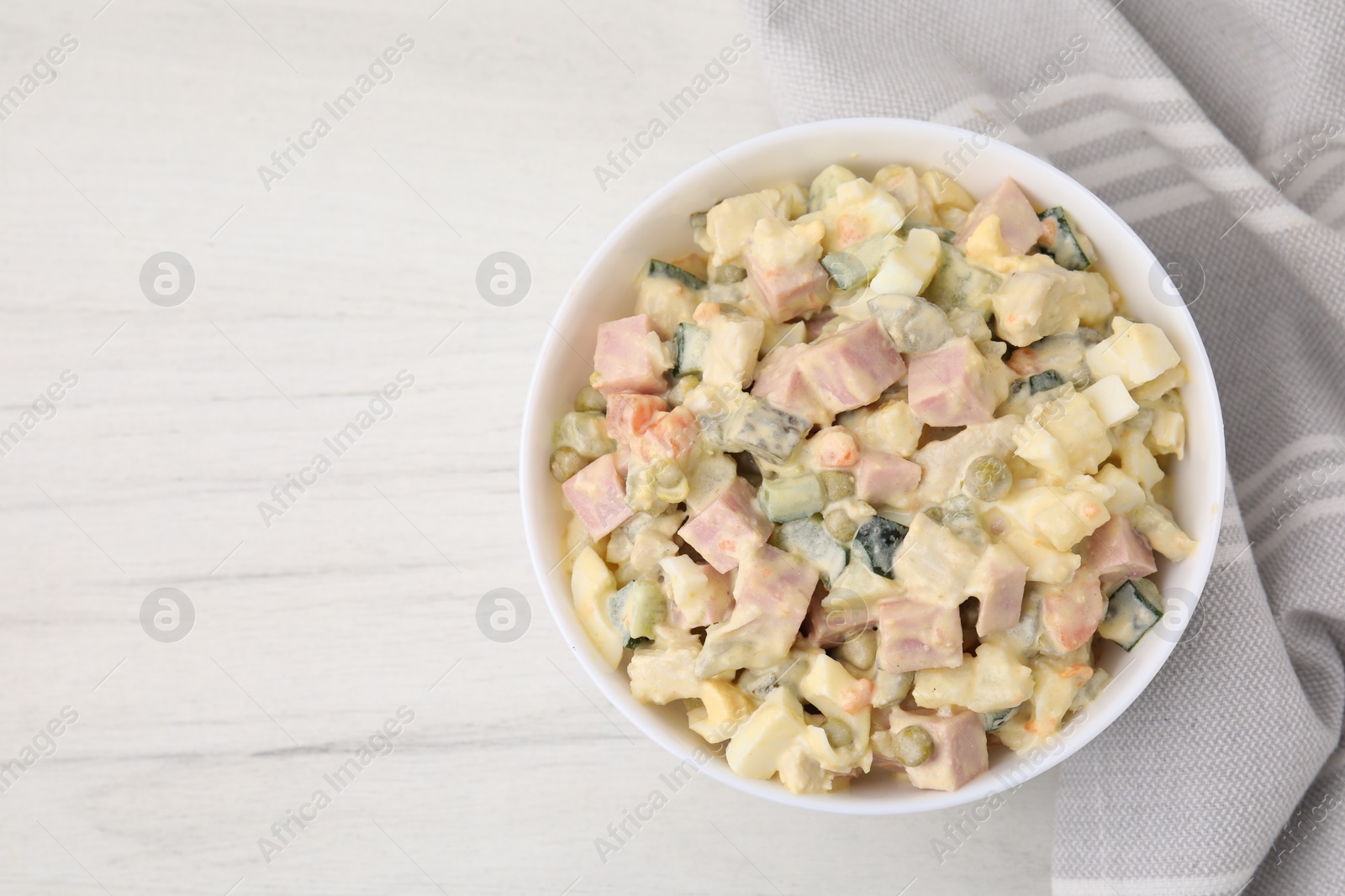 Photo of Tasty Olivier salad with boiled sausage in bowl on white wooden table, top view. Space for text