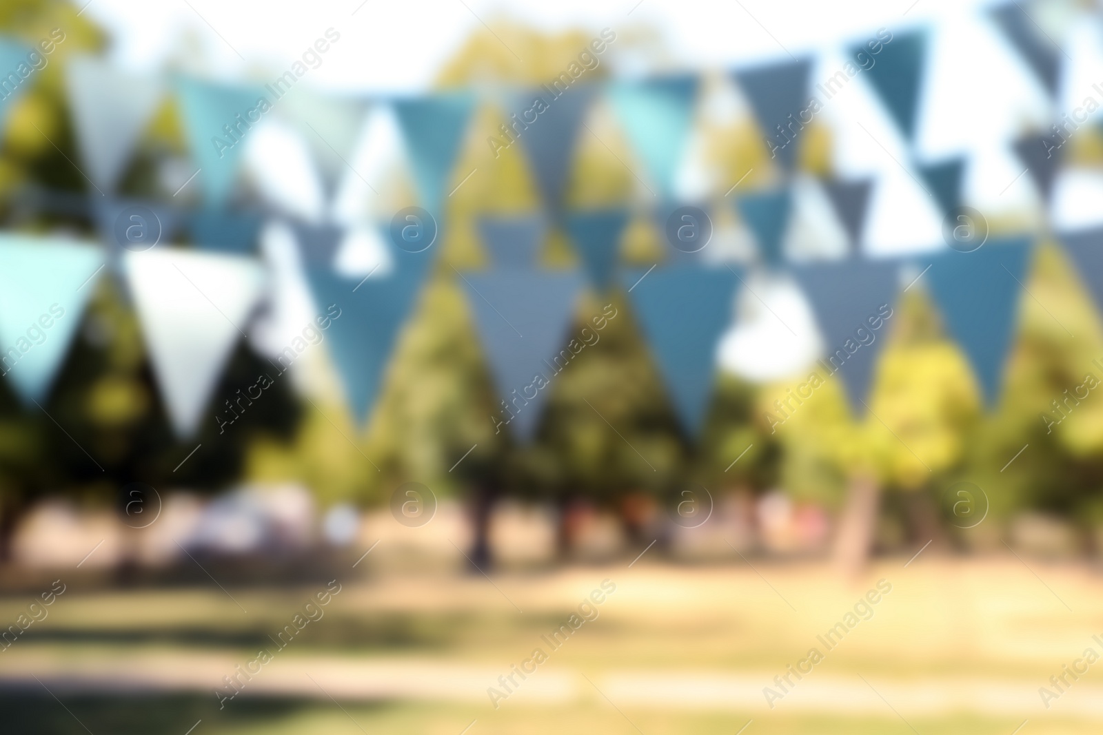 Photo of Blurred view of light blue bunting flags in park. Party decor