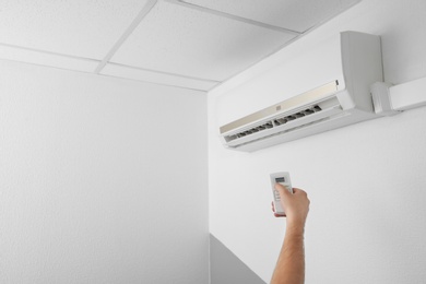 Man operating air conditioner with remote control indoors