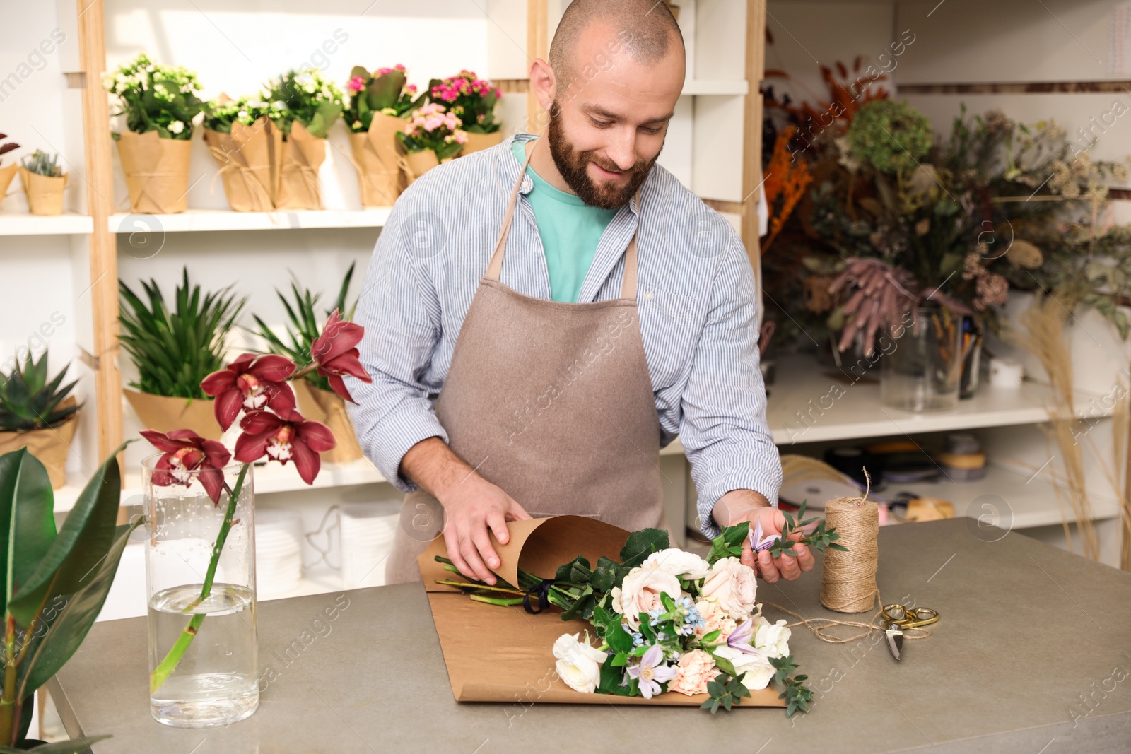 Photo of Florist making bouquet with fresh flowers at table in shop