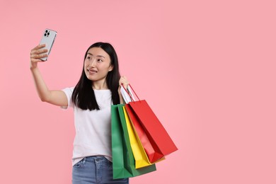 Photo of Smiling woman with shopping bags taking selfie on pink background. Space for text