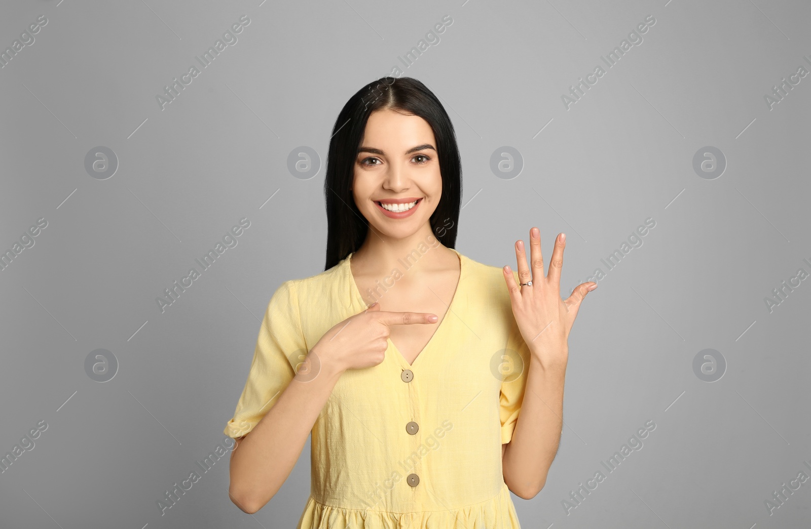 Photo of Happy young woman wearing beautiful engagement ring on grey background