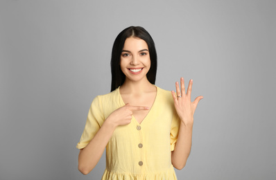 Photo of Happy young woman wearing beautiful engagement ring on grey background