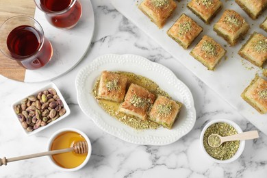 Photo of Delicious fresh baklava with chopped nuts and honey served on white marble table, flat lay. Eastern sweets