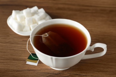 Photo of Tea bag in cup of hot water on wooden table