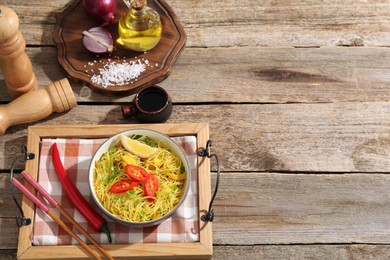 Photo of Stir-fry. Tasty noodles with vegetables and meat in bowl served on wooden table, flat lay. Space for text