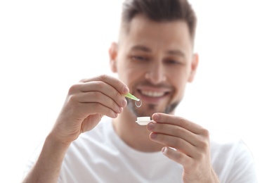 Young man holding contact lens with case on light background