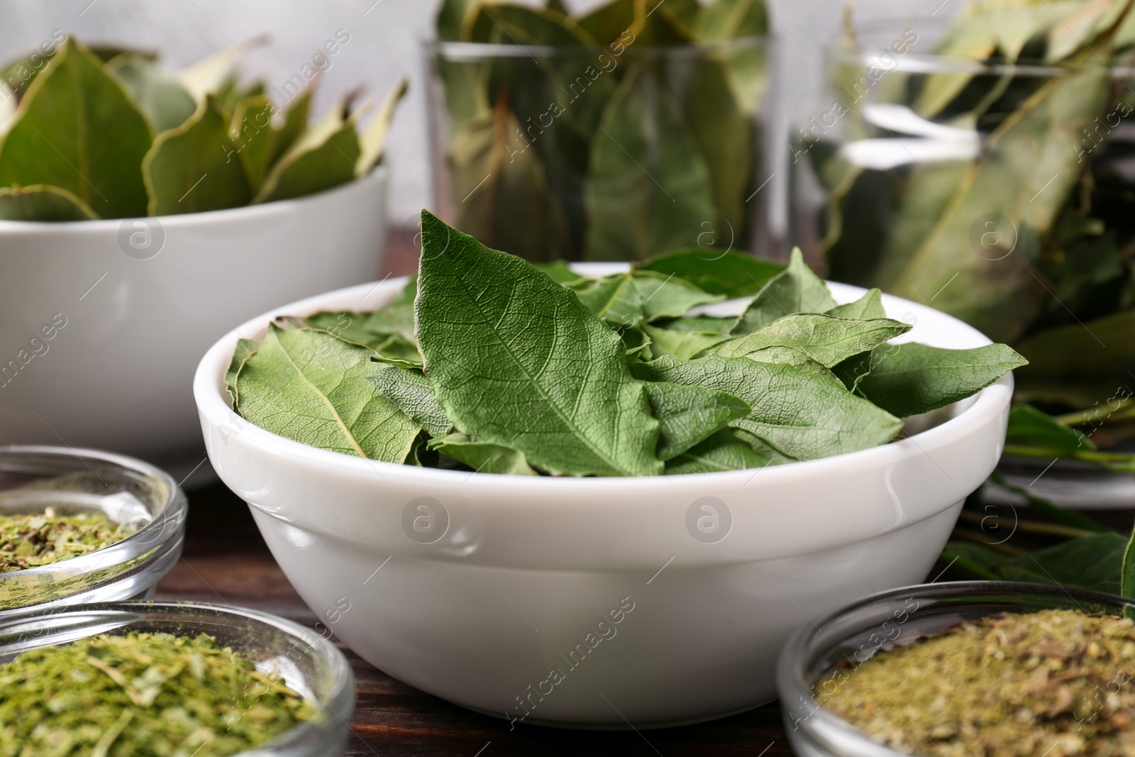 Photo of Bowls with ground, fresh and dry bay leaves on wooden table, closeup