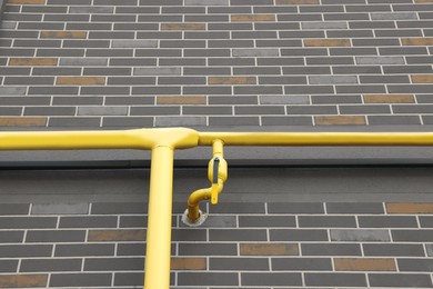 Photo of Yellow gas pipe with valve near brick wall outdoors, low angle view