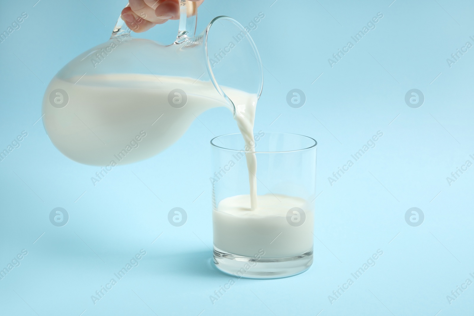 Photo of Woman pouring milk into glass on light blue background, closeup