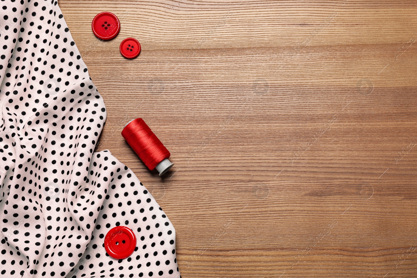 Photo of Fabric, red thread and buttons on wooden background, flat lay. Space for text