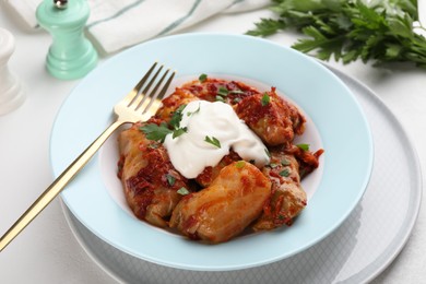 Delicious stuffed cabbage rolls served with sour cream on white table, closeup