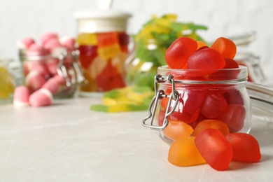 Glass jar with tasty jelly candies on light table, space for text