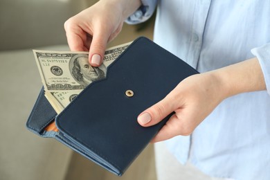 Photo of Money exchange. Woman putting dollar banknotes into wallet on blurred background, closeup