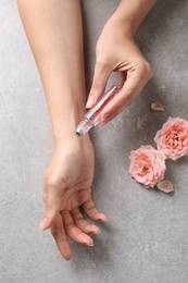 Photo of Woman applying rose essential oil on wrist and flowers at grey table, top view
