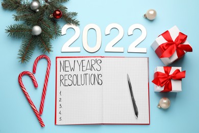 Photo of Making resolutions for 2022 New Year. Flat lay composition with notebook and festive decor on light blue background