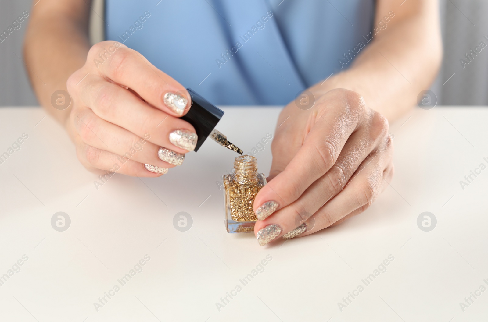 Photo of Woman applying nail polish at table, closeup. At-home manicure