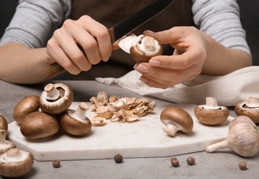 Photo of Young woman peeling fresh champignon mushrooms at table, closeup