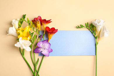 Photo of Beautiful spring freesia flowers and blank card on beige background, flat lay. Space for text