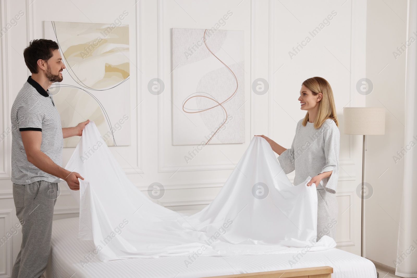 Photo of Couple changing bed linens in room. Domestic chores