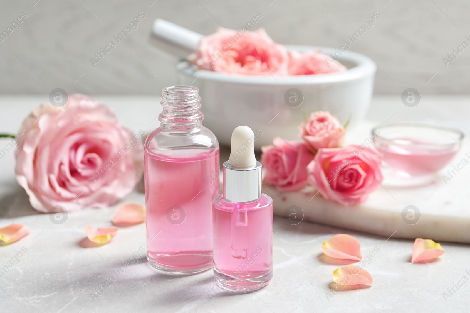 Photo of Bottles of rose essential oil and fresh flowers on table