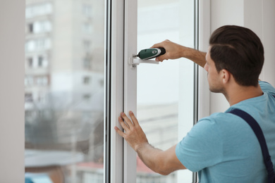 Construction worker repairing plastic window with electric screwdriver indoors