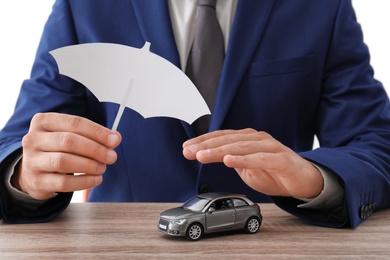 Photo of Insurance agent covering toy car with paper cutout umbrella and hand at table, closeup