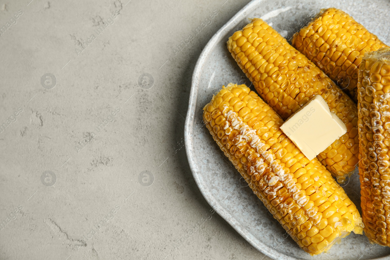 Photo of Delicious grilled corn with butter on light grey table, top view. Space for text