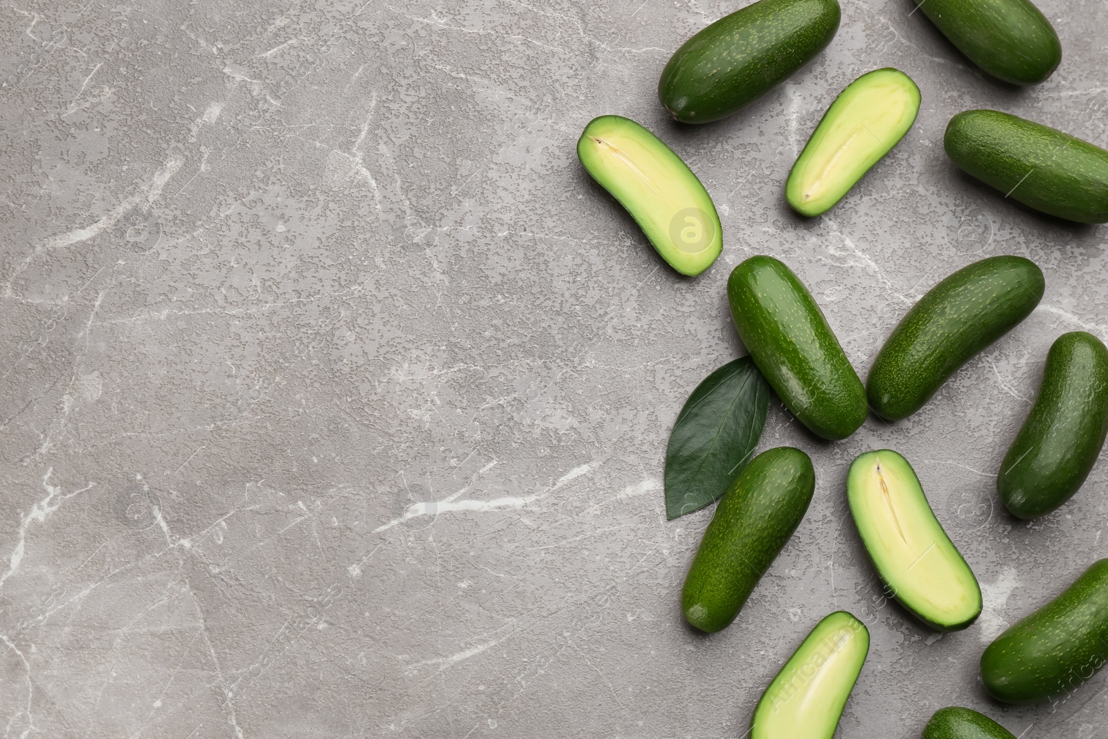 Photo of Fresh seedless avocados with green leaves on grey table, flat lay. Space for text