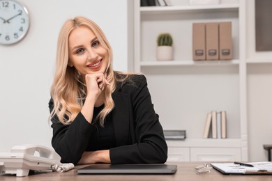 Happy secretary at table in office, space for text