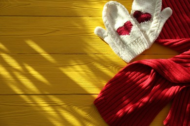 Red knitted scarf and mittens on yellow wooden table, top view. Space for text