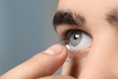 Photo of Closeup view of young man putting in contact lens on grey background