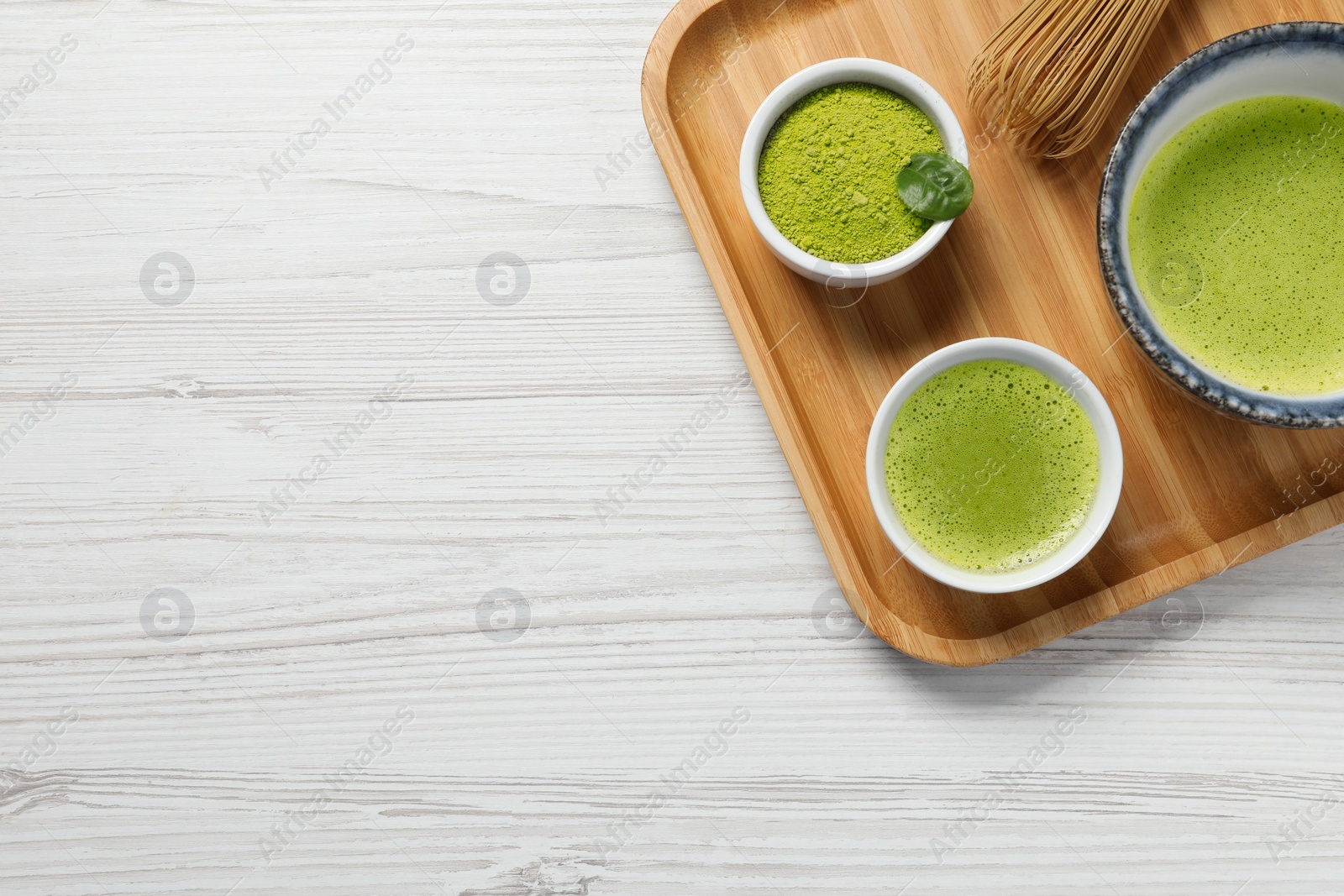 Photo of Fresh matcha tea, bamboo whisk and green powder on white wooden table, top view. Space for text