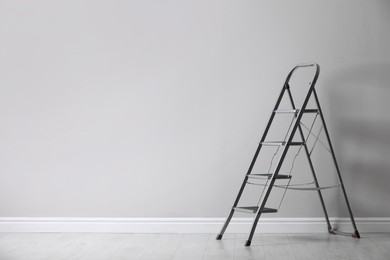 Photo of Modern metal stepladder near white wall indoors. Space for text