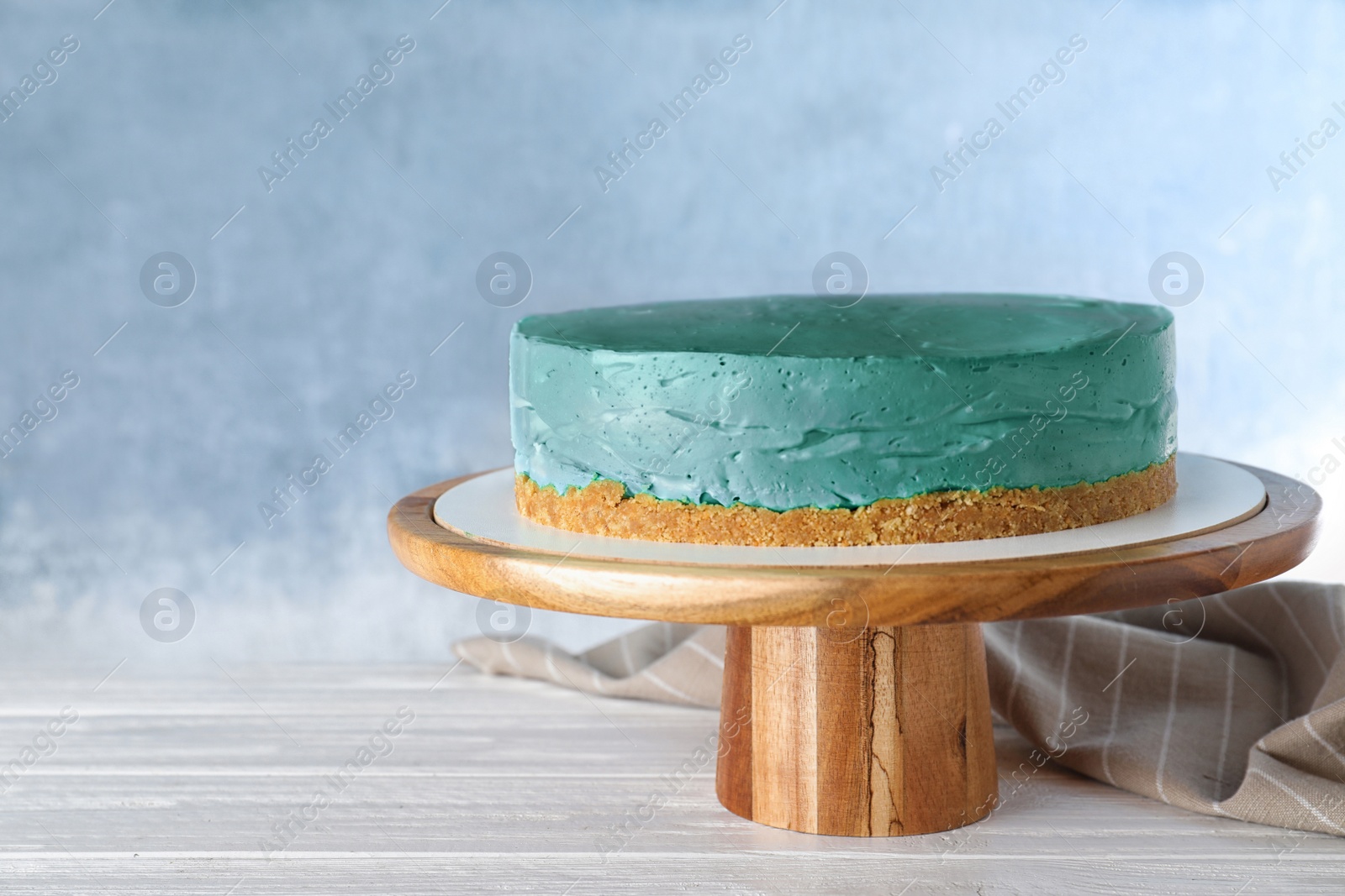 Photo of Delicious homemade spirulina cheesecake on white wooden table against blue background. Space for text