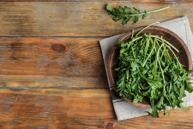 Photo of Fresh arugula in bowl on wooden table, flat lay. Space for text