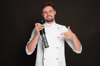 Photo of Smiling chef pointing on sous vide cooker against black background