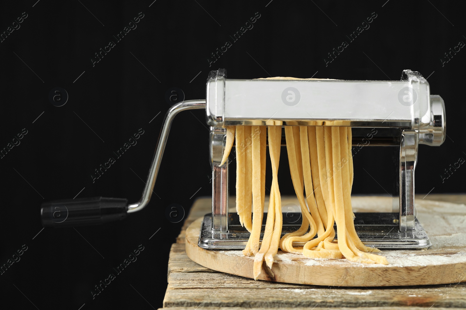 Photo of Pasta maker with raw dough on wooden table against black background, closeup