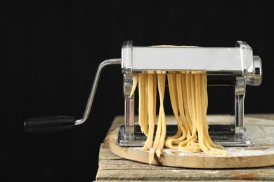 Photo of Pasta maker with raw dough on wooden table against black background, closeup