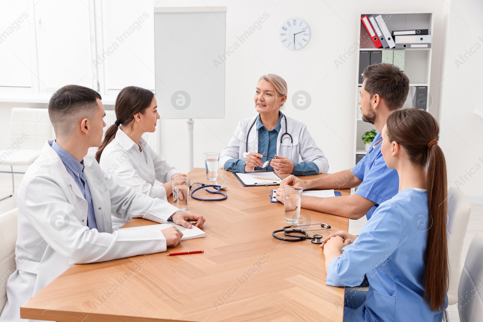 Photo of Medical conference. Team of doctors listening to speaker at wooden table in clinic