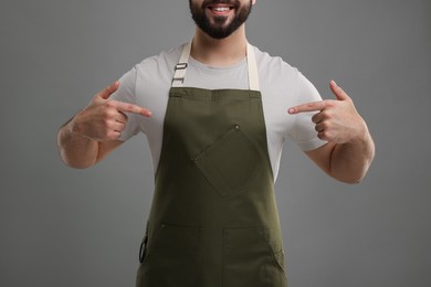 Smiling man pointing at kitchen apron on grey background, closeup. Mockup for design