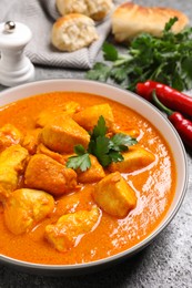 Photo of Bowl of delicious chicken curry on grey table, closeup