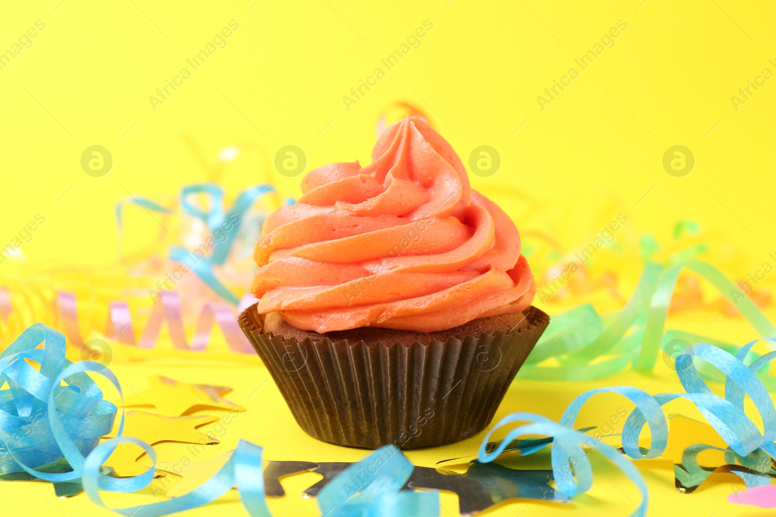 Photo of Delicious cupcake with bright cream and party decor on yellow background