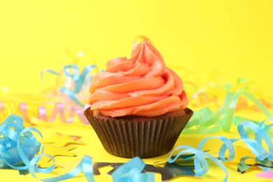 Photo of Delicious cupcake with bright cream and party decor on yellow background