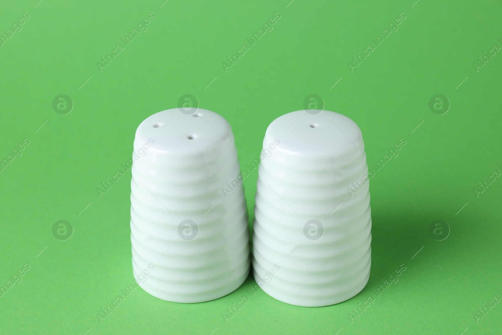 Photo of Salt and pepper shakers on green background, closeup