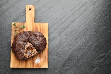 Photo of Piece of delicious grilled beef meat, thyme and salt on black table, top view. Space for text