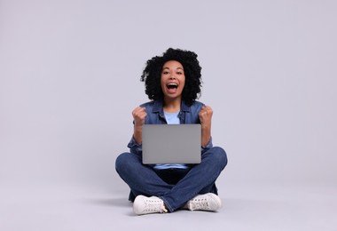 Emotional young woman with laptop on light grey background